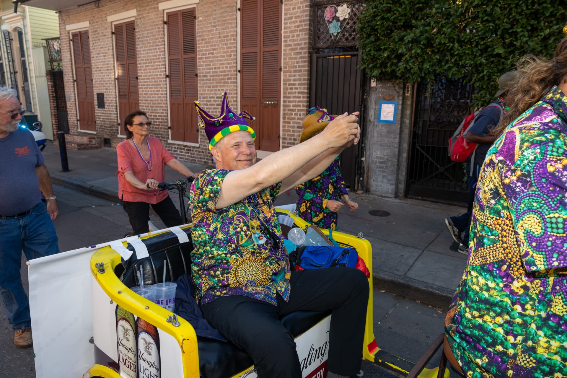 Randy waving from a decorated pedicab wearing a purple and gold jester crown